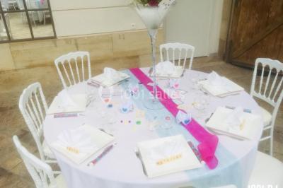 Table ronde décorée pour un événement, avec nappes blanches, chemin de table rose et bleu, et vaisselle élégante.