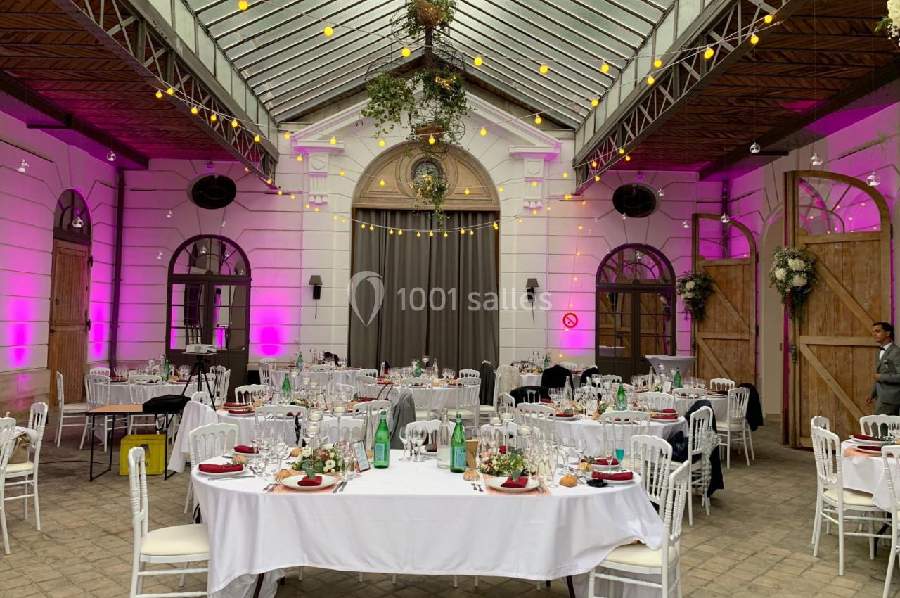 Salle de réception décorée avec des tables dressées, éclairage tamisé et guirlandes lumineuses suspendues.