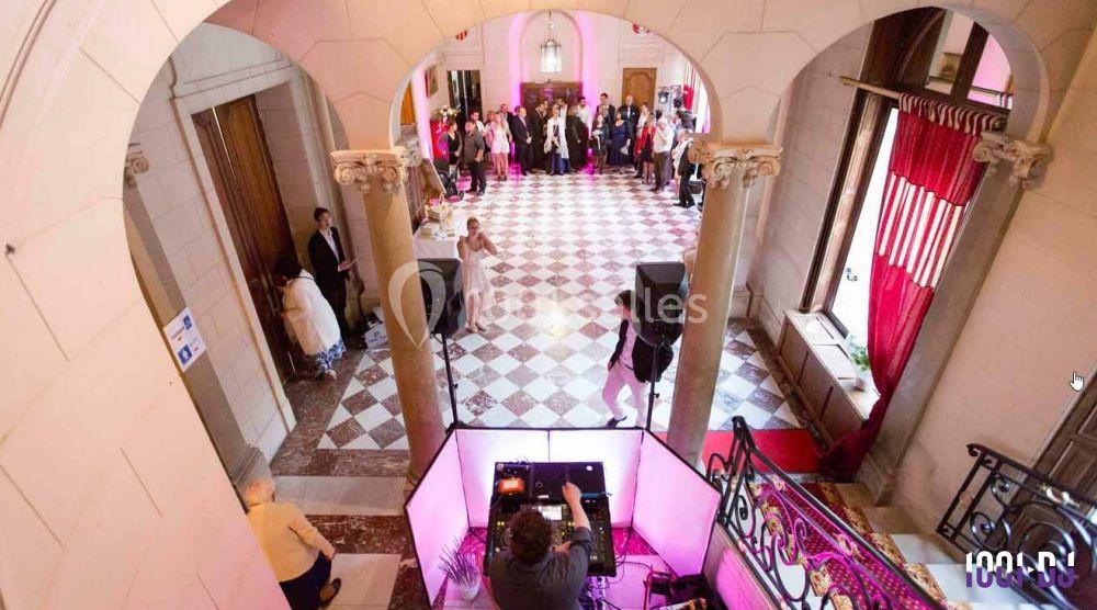 Vue d'une réception dans un hall élégant avec carrelage en damier, un DJ en bas et des invités debout en arrière-plan.