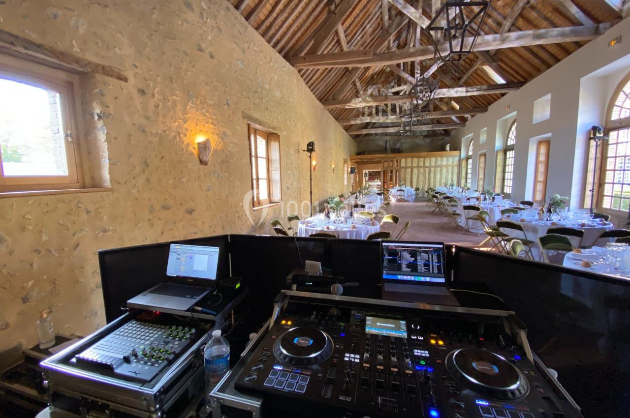 Console de DJ avec équipements audio dans une salle de réception lumineuse, décorée pour un événement.