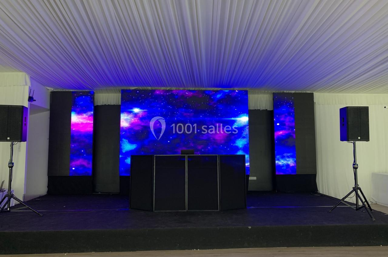 Scène avec écran LED affichant un fond étoilé violet et bleu, entourée de haut-parleurs sous une tente blanche.