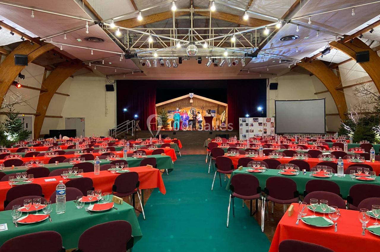 Salle décorée avec des tables dressées en rouge et vert, face à une scène éclairée avec des artistes en représentation.