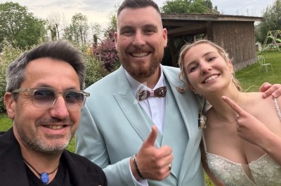Un DJ souriant anime une soirée dansante dans une salle éclairée par des lumières colorées, avec des invités sur la piste.