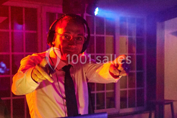 Homme en chemise et cravate portant un casque audio, pointant vers l'objectif dans une ambiance lumineuse colorée.