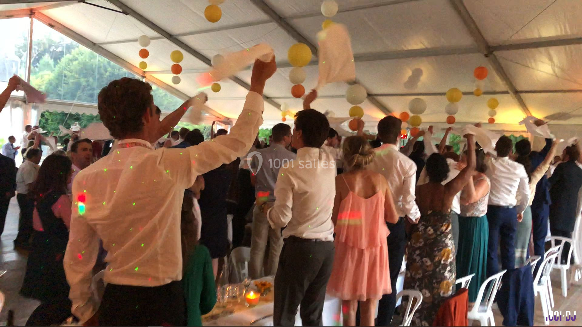 Des invités debout sous une tente festive agitent des serviettes blanches lors d'un événement convivial.