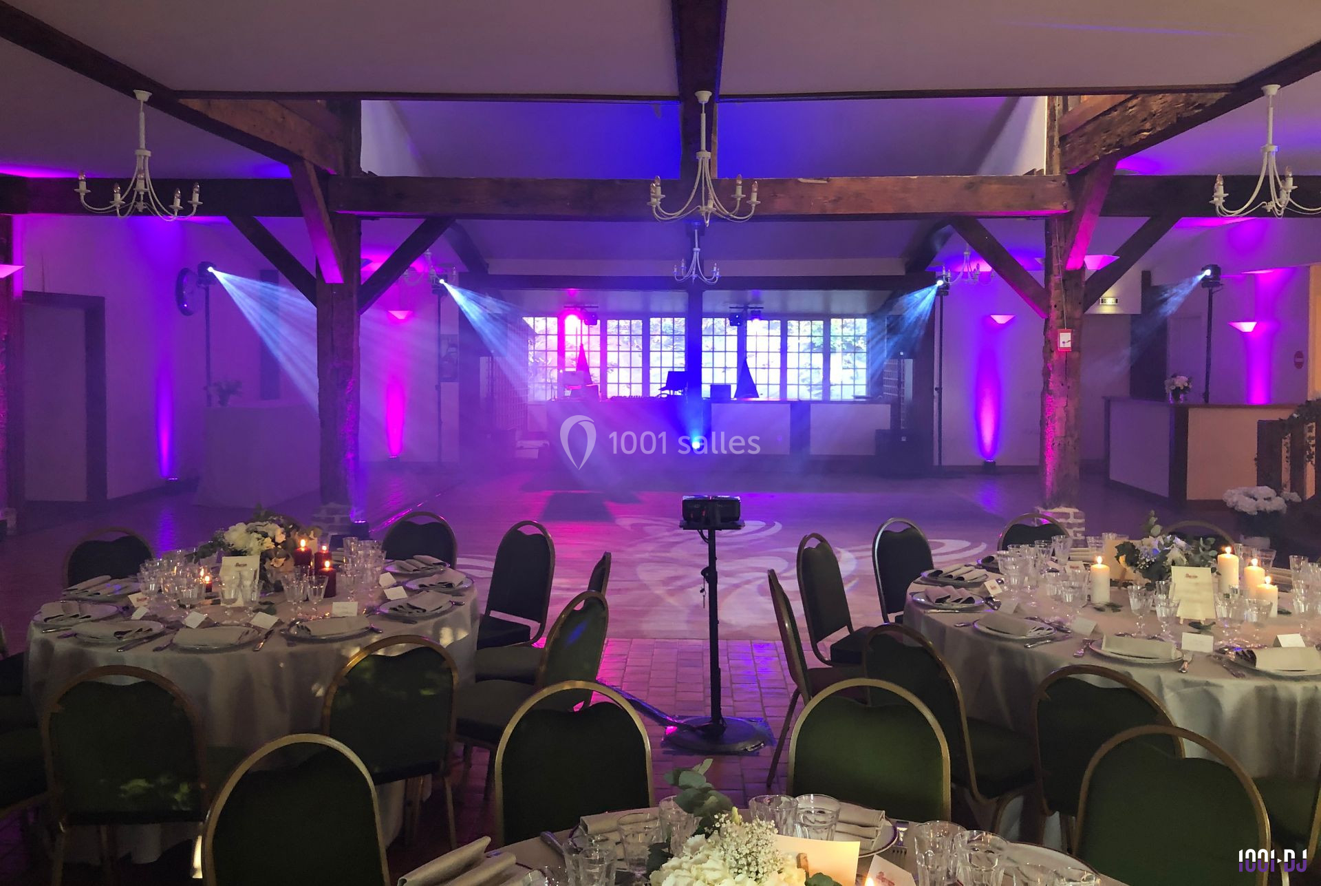 Salle de réception décorée avec tables dressées, éclairages colorés et piste de danse vide au centre.
