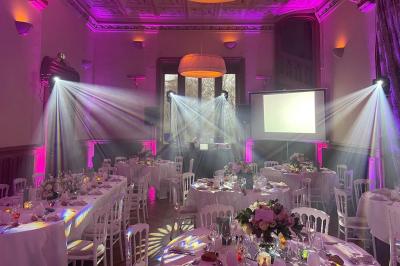Une femme en robe blanche joue de la harpe dans une salle décorée avec des plantes et des lumières.