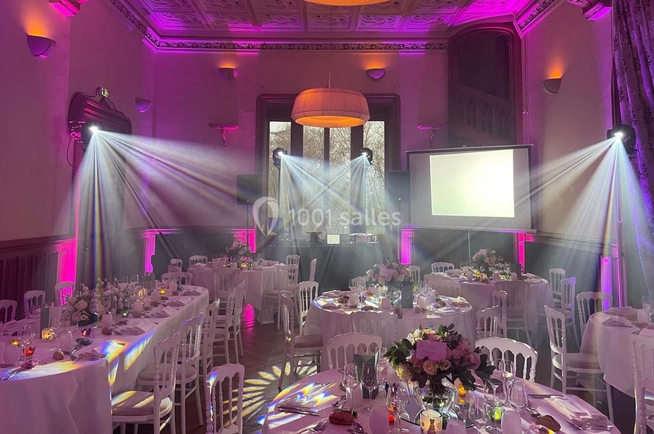 Salle de réception décorée avec des tables dressées, éclairage rose et projecteurs créant une ambiance festive.