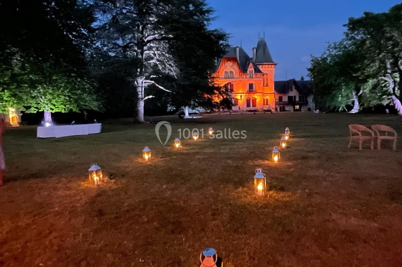 Allée de lanternes éclairées menant à un château illuminé en orange, entouré d'arbres au crépuscule.