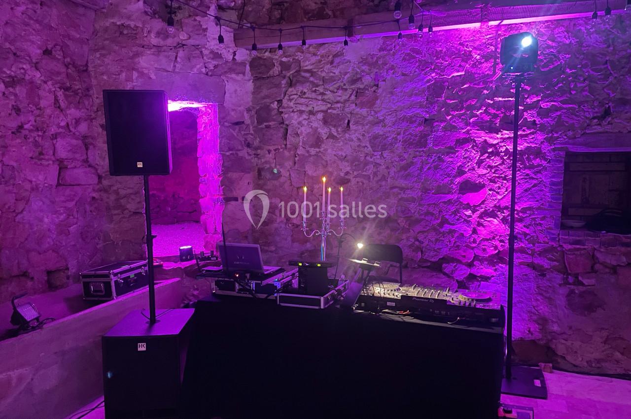 Installation de matériel de DJ avec table de mixage et éclairage violet dans une salle en pierre.