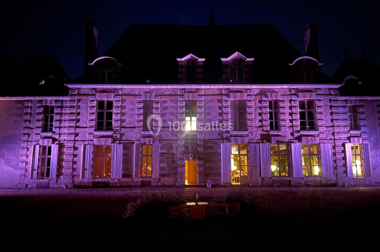 Façade d'un bâtiment ancien éclairée par des lumières violettes et jaunes dans l'obscurité.
