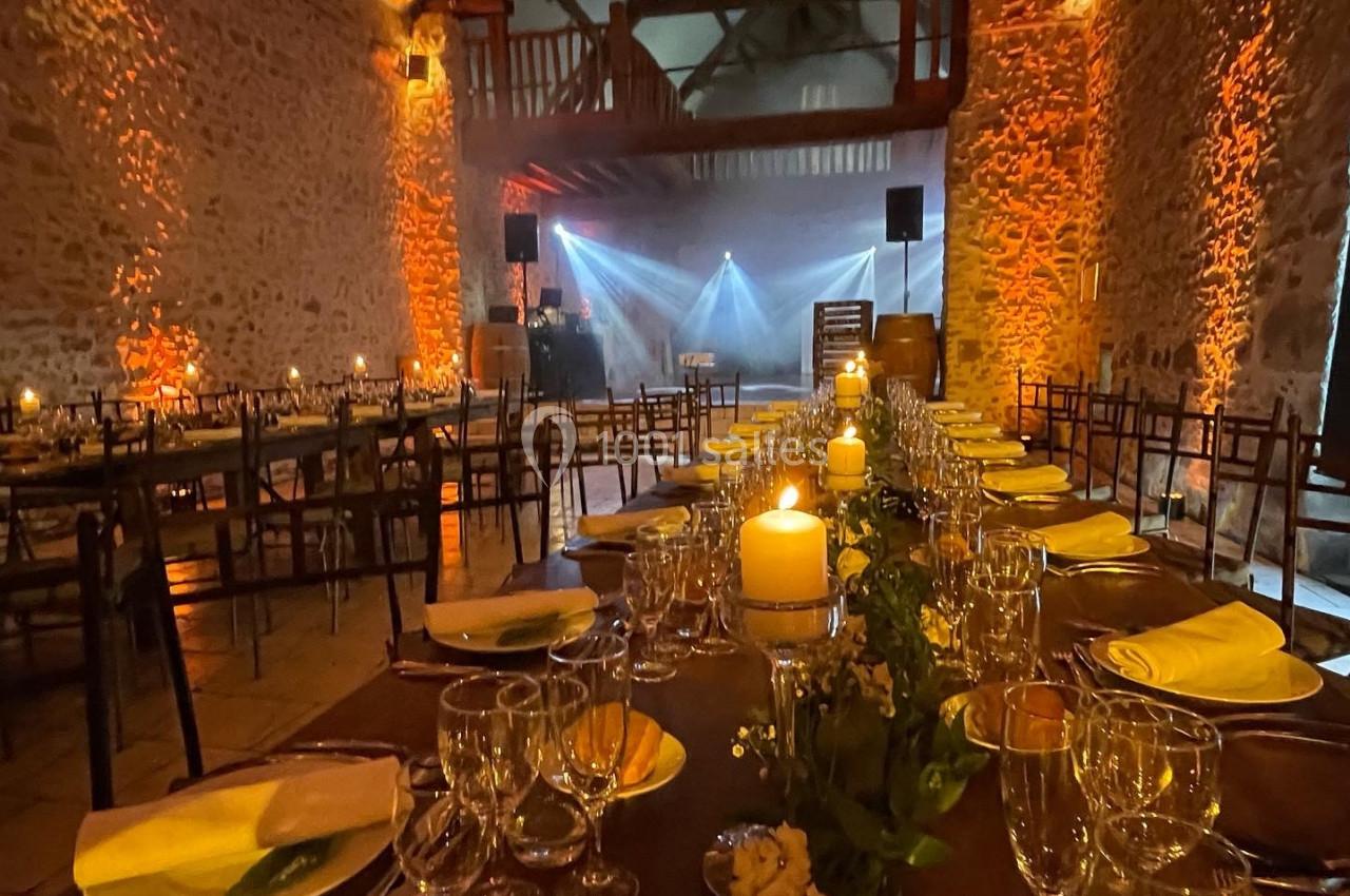 Salle de réception en pierre éclairée, avec tables dressées, chandelles et lumières d'ambiance chaleureuses.