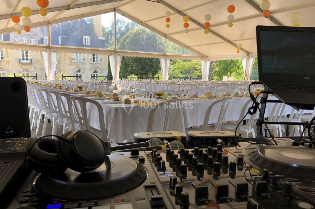 Tables dressées pour un événement sous une tente, avec une console de DJ au premier plan et un bâtiment en arrière-plan.