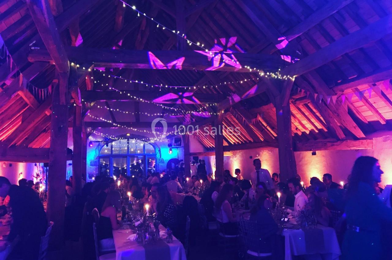 Salle de réception en soirée avec invités attablés, éclairage tamisé et guirlandes lumineuses suspendues.