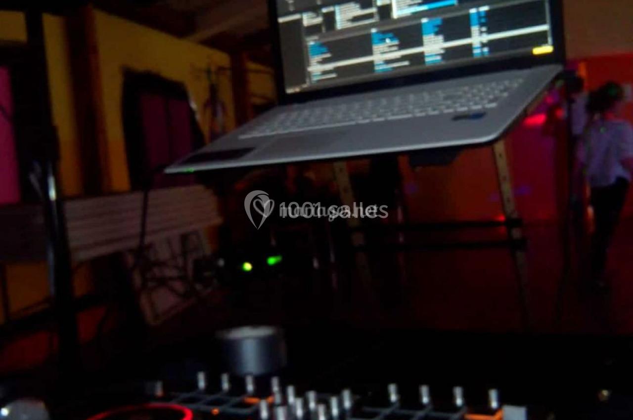 Console de mixage DJ avec un ordinateur portable affichant un logiciel de musique, dans un environnement sombre.