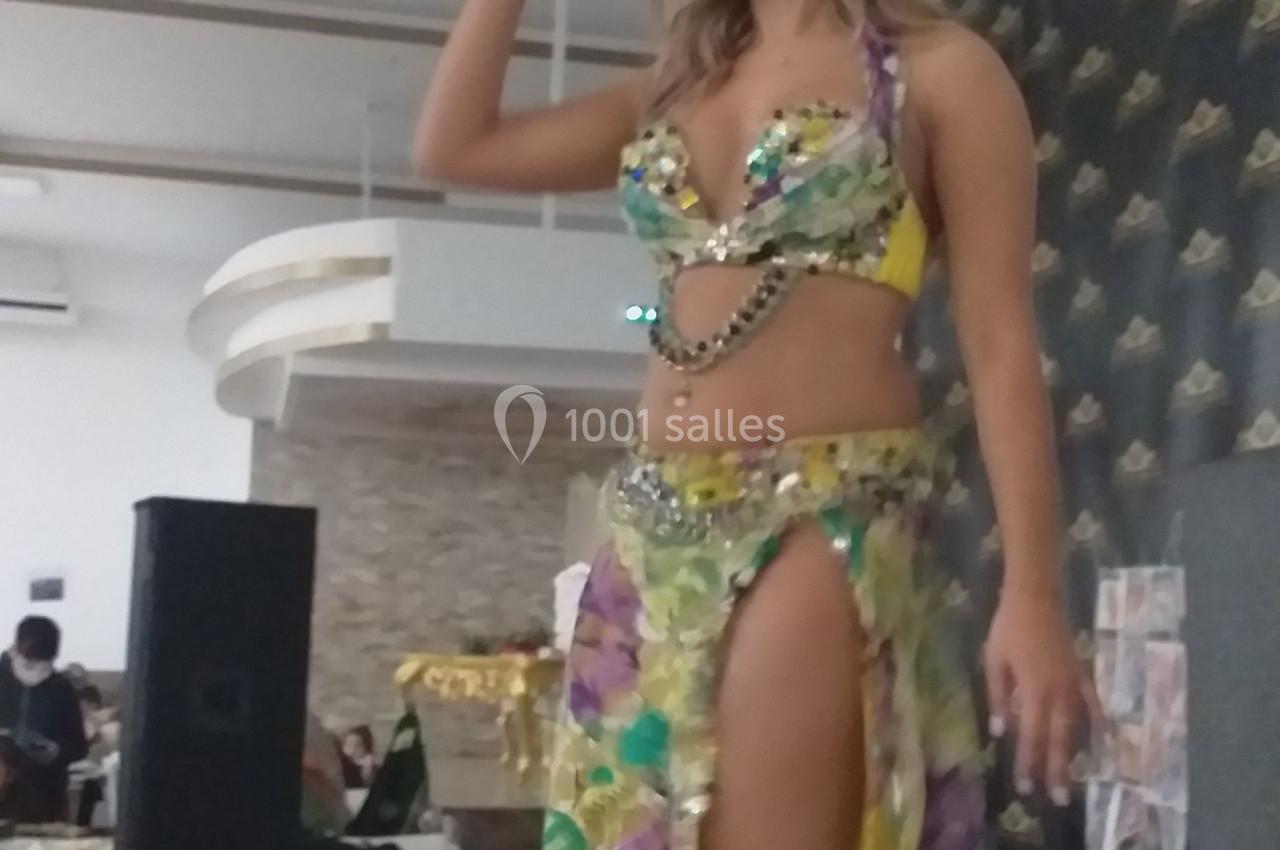 Une danseuse en tenue colorée de danse orientale se produit dans une salle lumineuse avec un décor moderne.