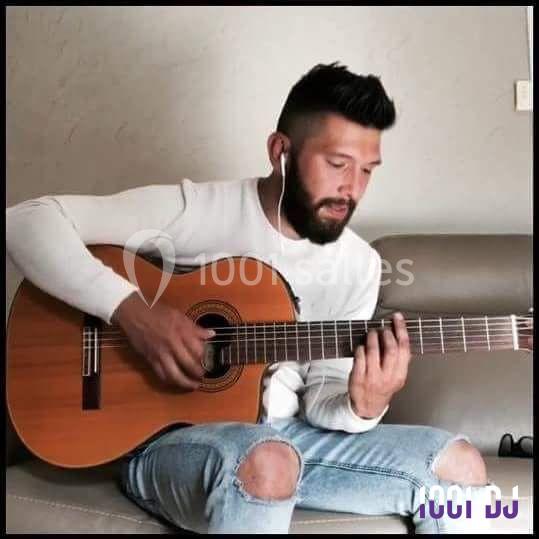 Un homme assis sur un canapé joue de la guitare acoustique tout en écoutant avec des écouteurs.
