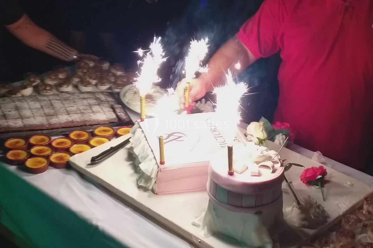 Gâteau décoré avec bougies étincelantes sur une table garnie de desserts variés, entourée de convives.