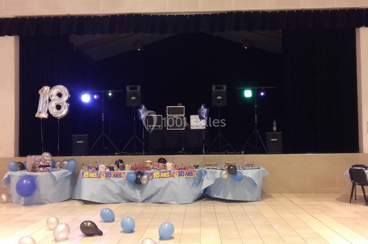 Salle décorée pour une fête d'anniversaire de 18 ans, avec ballons, tables garnies et matériel de sonorisation sur scène.