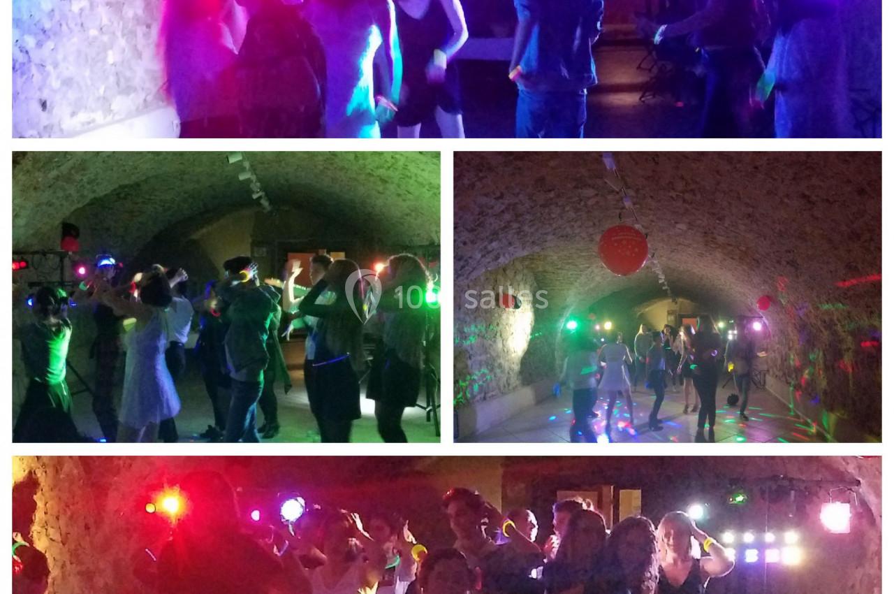 Personnes dansant sous des lumières colorées dans une salle voûtée en pierre.