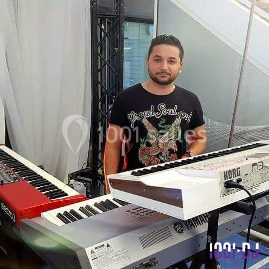 Un homme debout derrière plusieurs claviers électroniques dans un environnement intérieur.