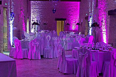 Salle de réception décorée avec des tables rondes dressées, des nappes blanches et des éclairages bleutés.