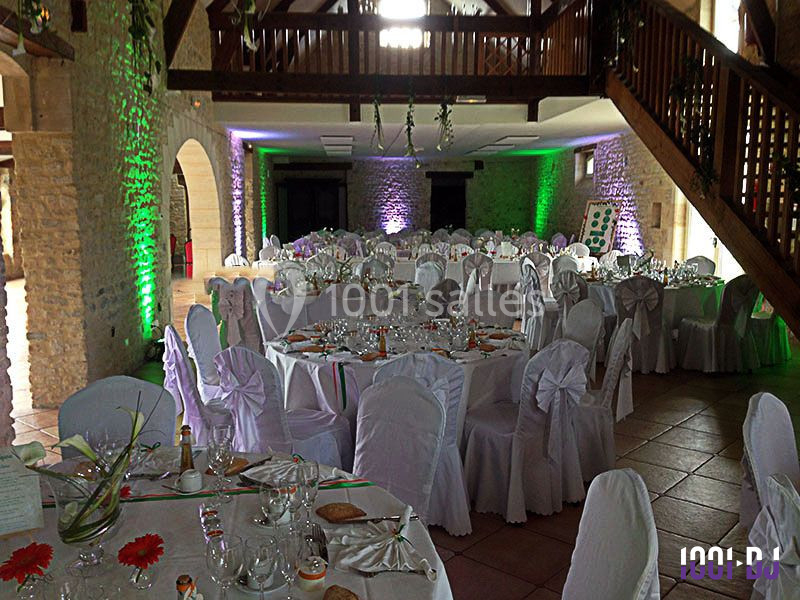Salle de réception décorée avec des tables rondes dressées, nappes blanches et éclairage coloré sur les murs en pierre.