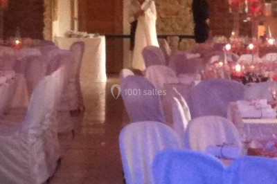 Salle de réception décorée avec des tables rondes dressées, des nappes blanches et des éclairages bleutés.