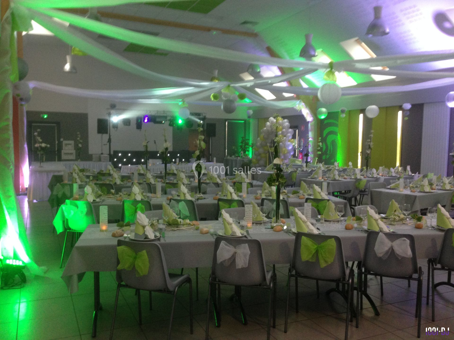 Salle de réception décorée en vert et blanc avec des tables dressées pour un événement festif.