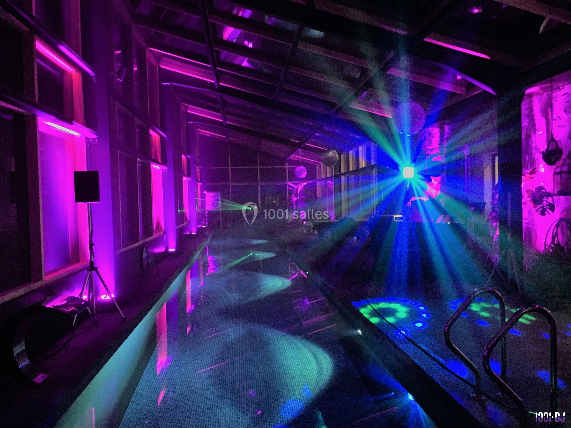 Piscine intérieure éclairée par des lumières colorées et des effets lumineux dans une ambiance nocturne.