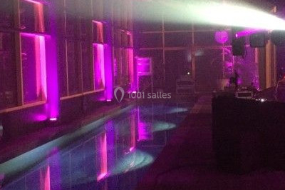 Salle de réception décorée avec des tables rondes dressées, des nappes blanches et des éclairages bleutés.