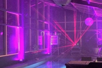 Salle de réception décorée avec des tables rondes dressées, des nappes blanches et des éclairages bleutés.