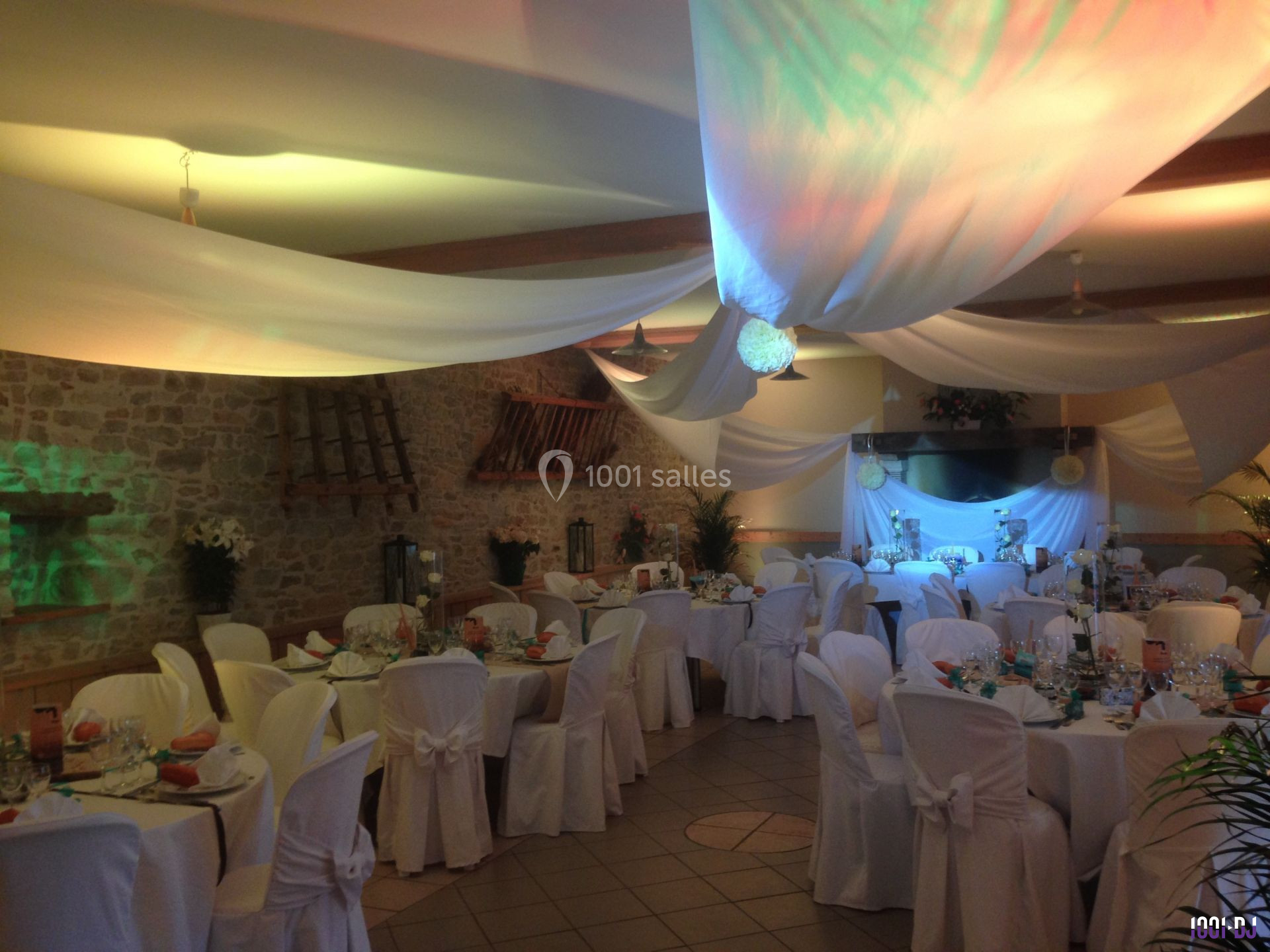Salle de réception décorée avec des nappes blanches, des tables dressées et un éclairage coloré.