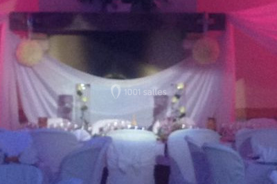 Salle de réception décorée avec des tables rondes dressées, des nappes blanches et des éclairages bleutés.