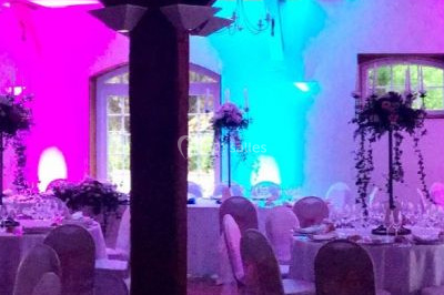 Salle de réception décorée avec des tables rondes dressées, des nappes blanches et des éclairages bleutés.