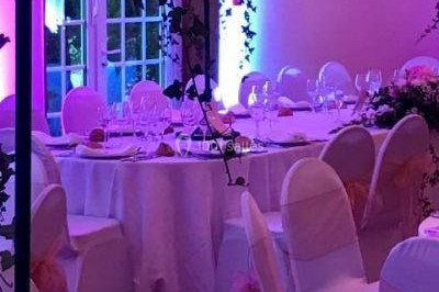 Salle de réception décorée avec des tables rondes dressées, des nappes blanches et des éclairages bleutés.