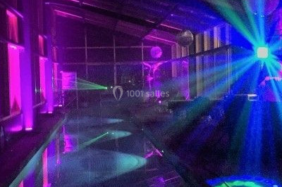 Salle de réception décorée avec des tables rondes dressées, des nappes blanches et des éclairages bleutés.