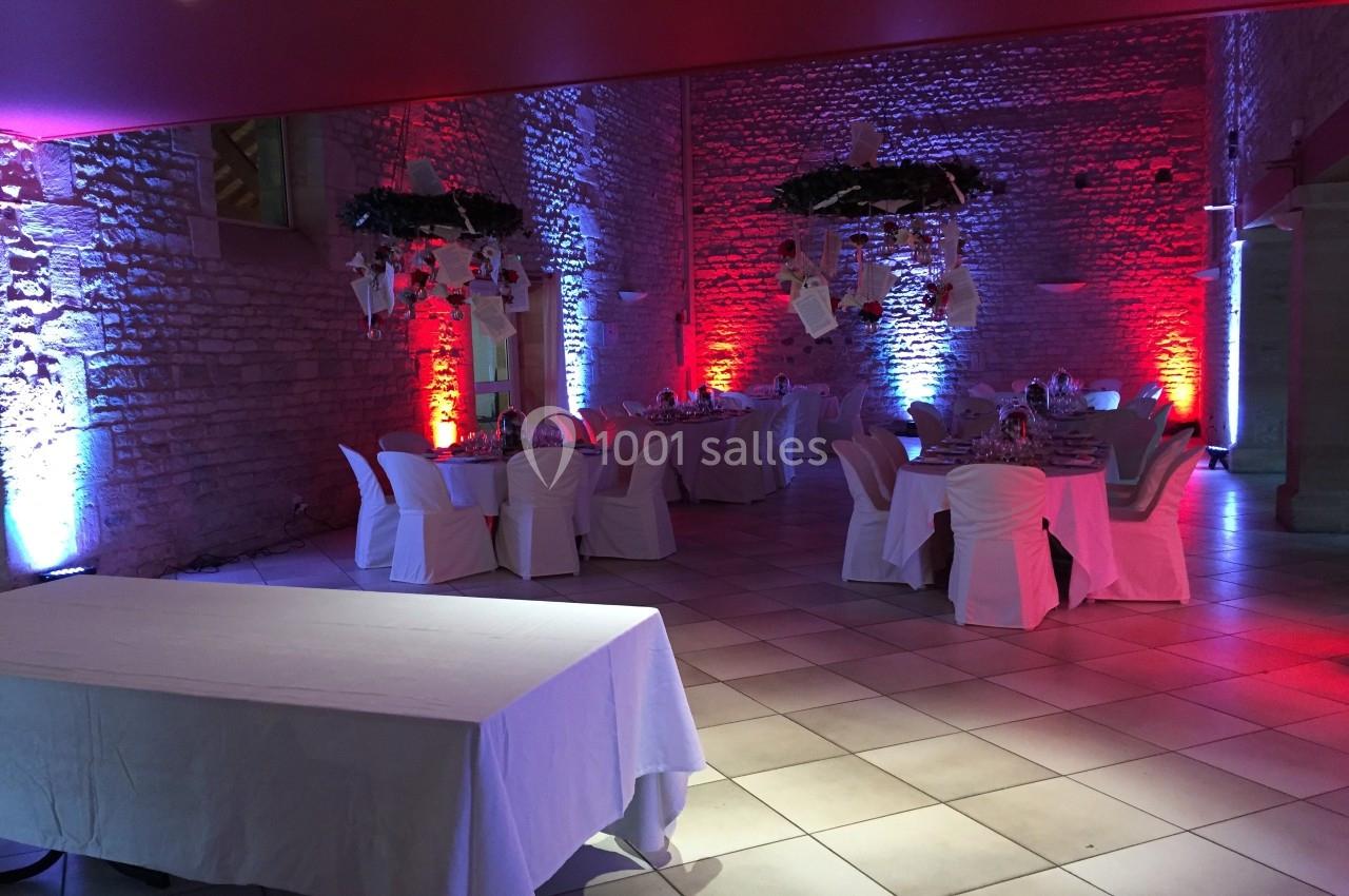 Salle de réception en pierre éclairée de lumières colorées, avec tables dressées et décorations suspendues.