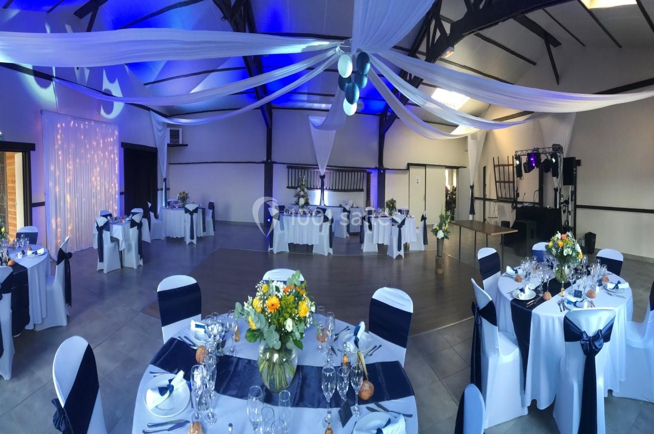 Salle de réception décorée avec des tables rondes dressées, des nappes blanches et des éclairages bleutés.