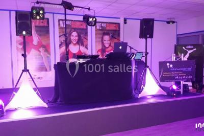 Scène éclairée avec une table de mixage, des enceintes et des affiches en arrière-plan dans une salle intérieure.