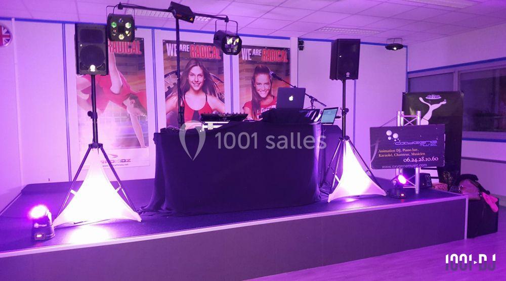 Scène éclairée avec une table de mixage, des enceintes et des affiches en arrière-plan dans une salle intérieure.