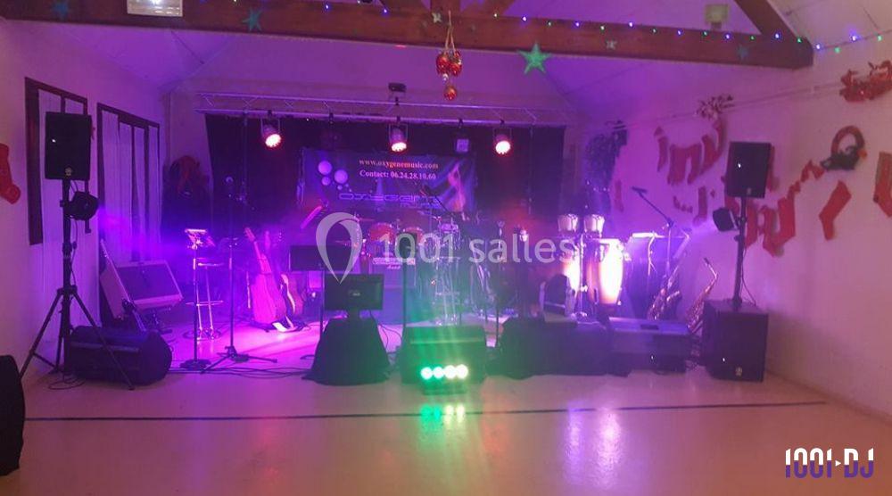 Scène de concert en intérieur avec instruments de musique, éclairage coloré et décorations suspendues.