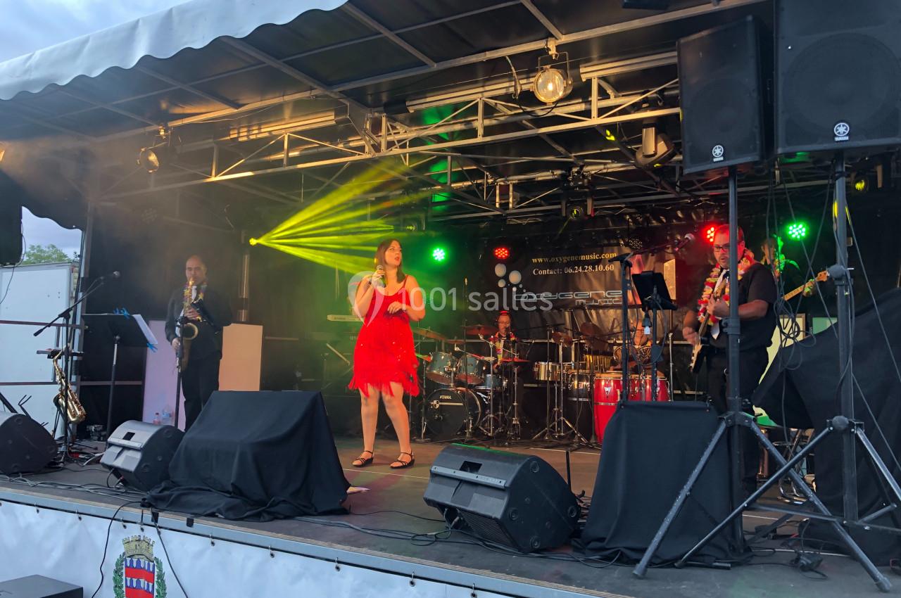 Groupe de musiciens et chanteuse en robe rouge se produisant sur une scène extérieure éclairée.