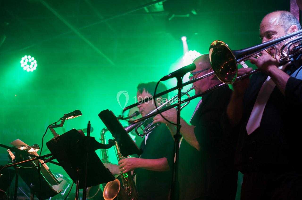 Musiciens jouant du trombone et du saxophone sur une scène éclairée par des lumières vertes.