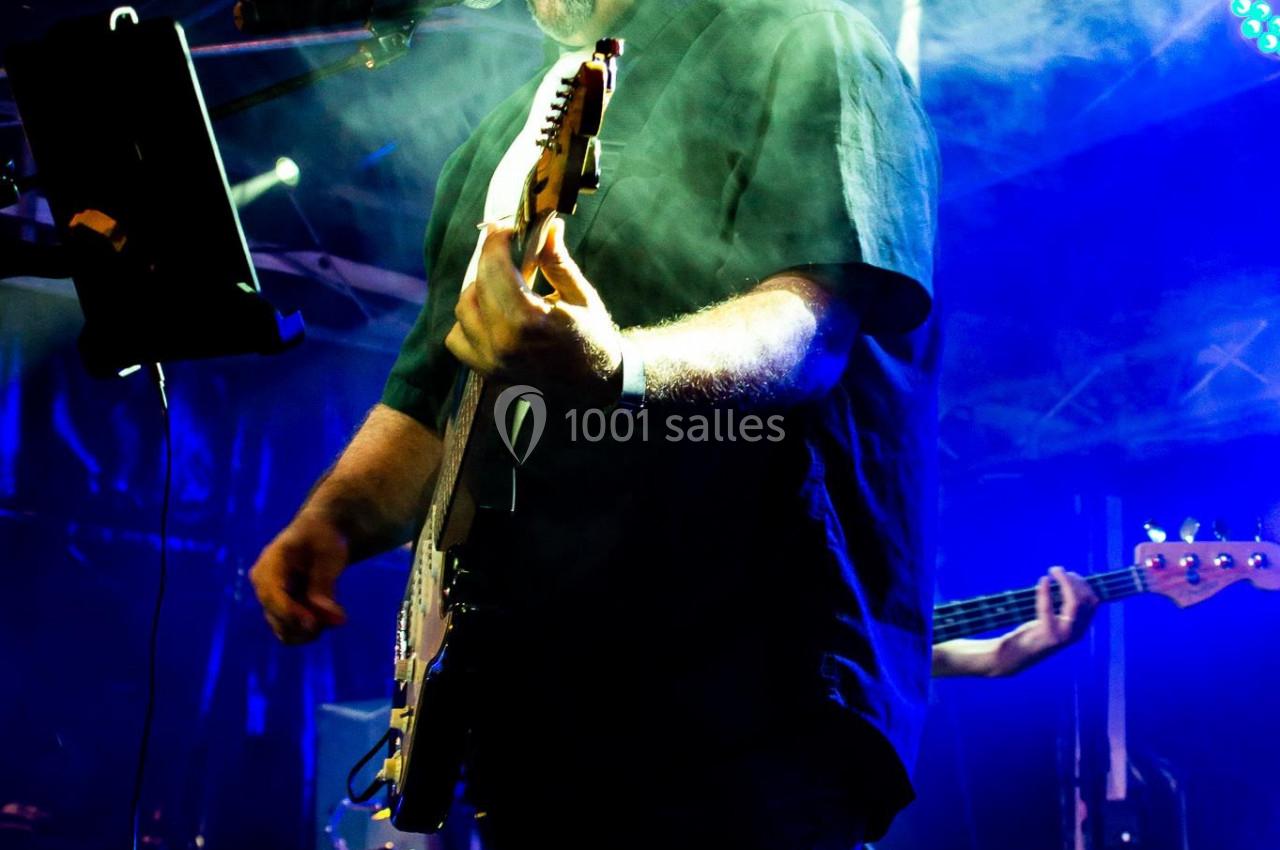 Un musicien joue de la guitare et chante sur une scène éclairée par des lumières colorées, entouré de fumée.