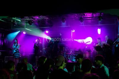 Scène de concert avec instruments et éclairages colorés dans une salle vide.