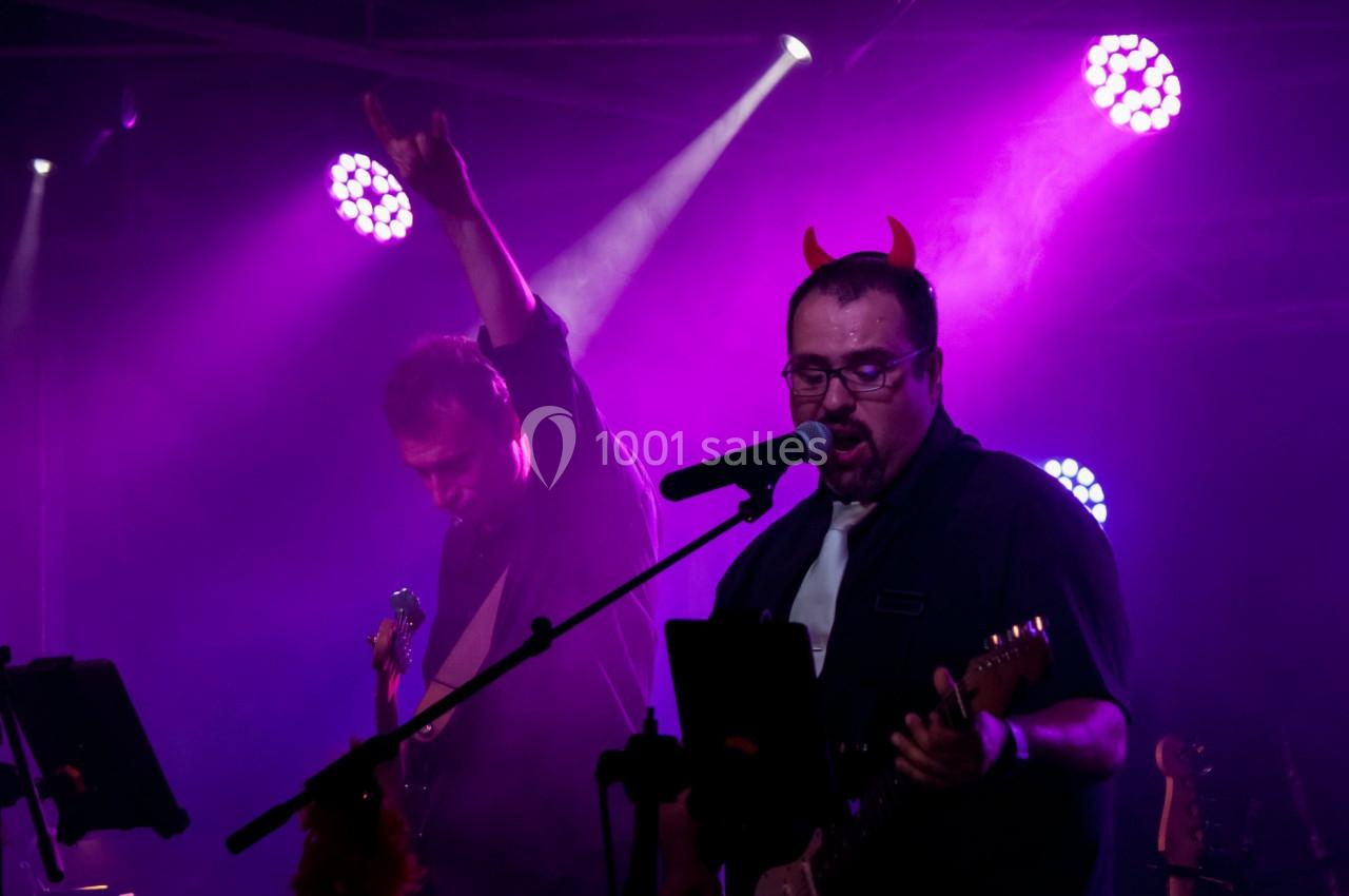 Deux musiciens sur scène sous des lumières violettes, l'un portant des cornes rouges et chantant au micro.