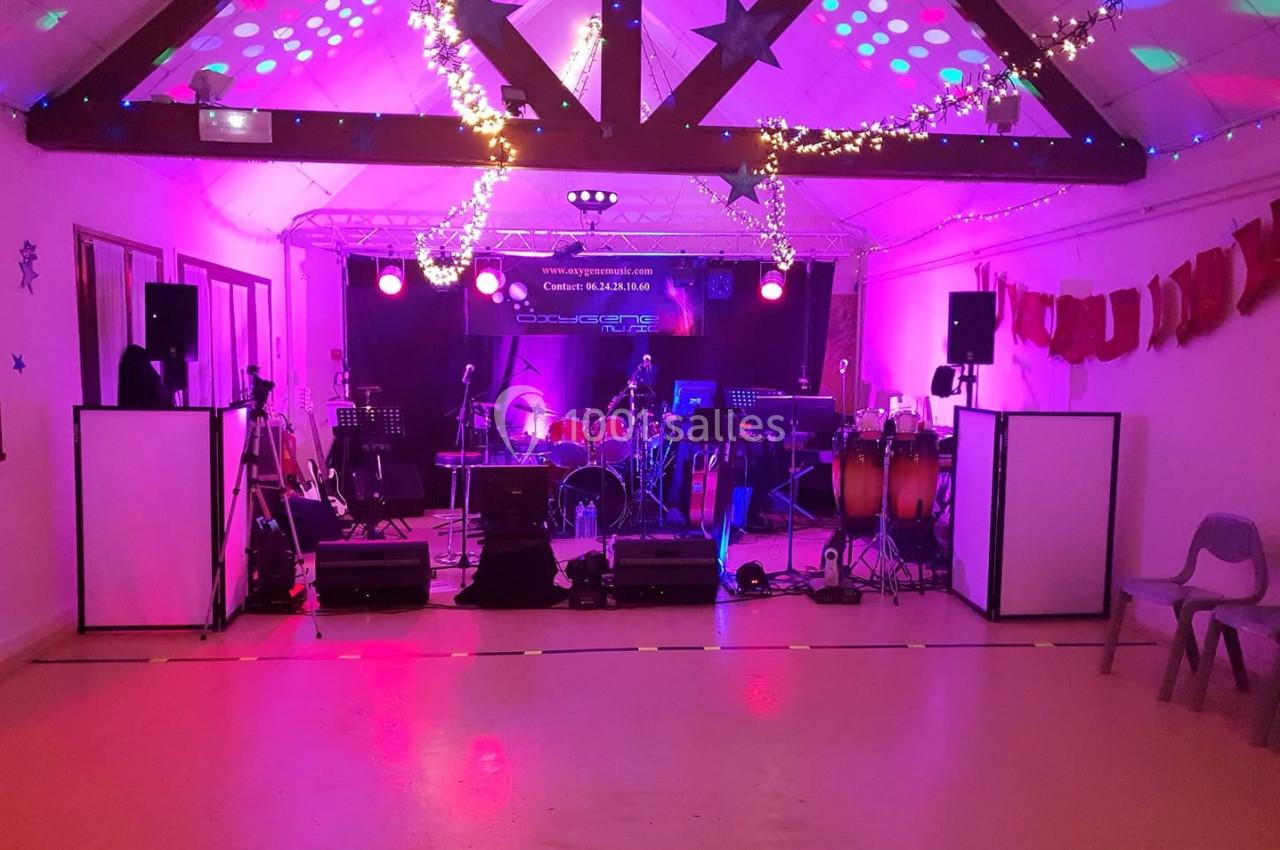 Salle décorée avec guirlandes lumineuses, scène équipée de matériel musical et éclairages colorés.