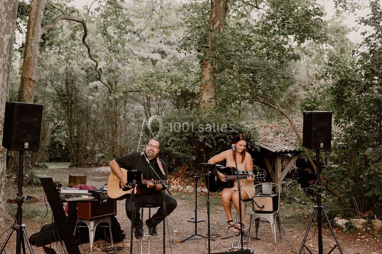 Deux musiciens jouant de la guitare acoustique en plein air, entourés d'arbres et d'équipements audio.