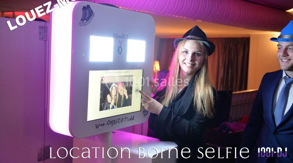 Femme souriante utilisant une borne photo interactive dans un environnement festif avec éclairage coloré.